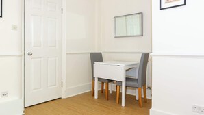 Une pièce avec une porte blanche, une table blanche avec des chaises, un tableau encadré au mur et un interrupteur sur le mur.
