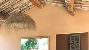 Una stanza con soffitto in paglia, un divano e una poltrona in vimini, una finestra vista sul verde e una porta con persiane.