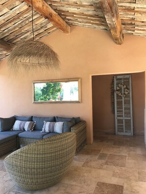A room with a thatched ceiling, a wicker sofa, a wicker chair, a window with a view of greenery, and a door with shutters. - Villa hauteur de Lauris infinity pool not overlooked (Lauris)