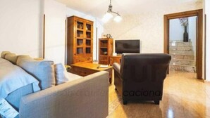 Uma sala de estar com sofá, uma poltrona, um armário de madeira, televisão e escada.