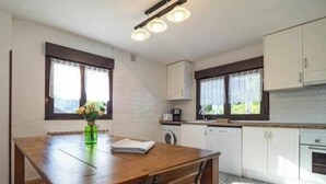 Uma cozinha com mesa de madeira, armários brancos e janela com cortinas.