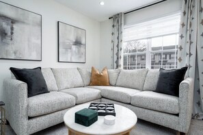 A modern living room with a grey sectional sofa, a round coffee table, and abstract wall art. - Modern Luxury Retreat 3BR/2.5 bath, 2 Decks, Near Christiana & Wilmington (New Castle)