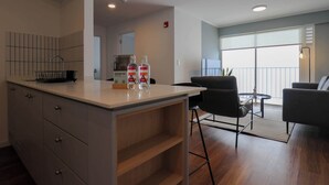 A modern kitchen with a white countertop, a black chair, and a dining table. There are two bottles on the counter. - w* | Central 2BR w/ Balcony in Miraflores (Miraflores)