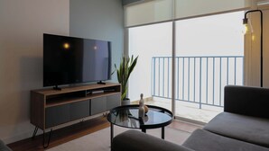A modern living room with a flat-screen TV, a glass coffee table, a sofa, a potted plant, and a balcony with a railing. - w* | Central 2BR w/ Balcony in Miraflores (Miraflores)