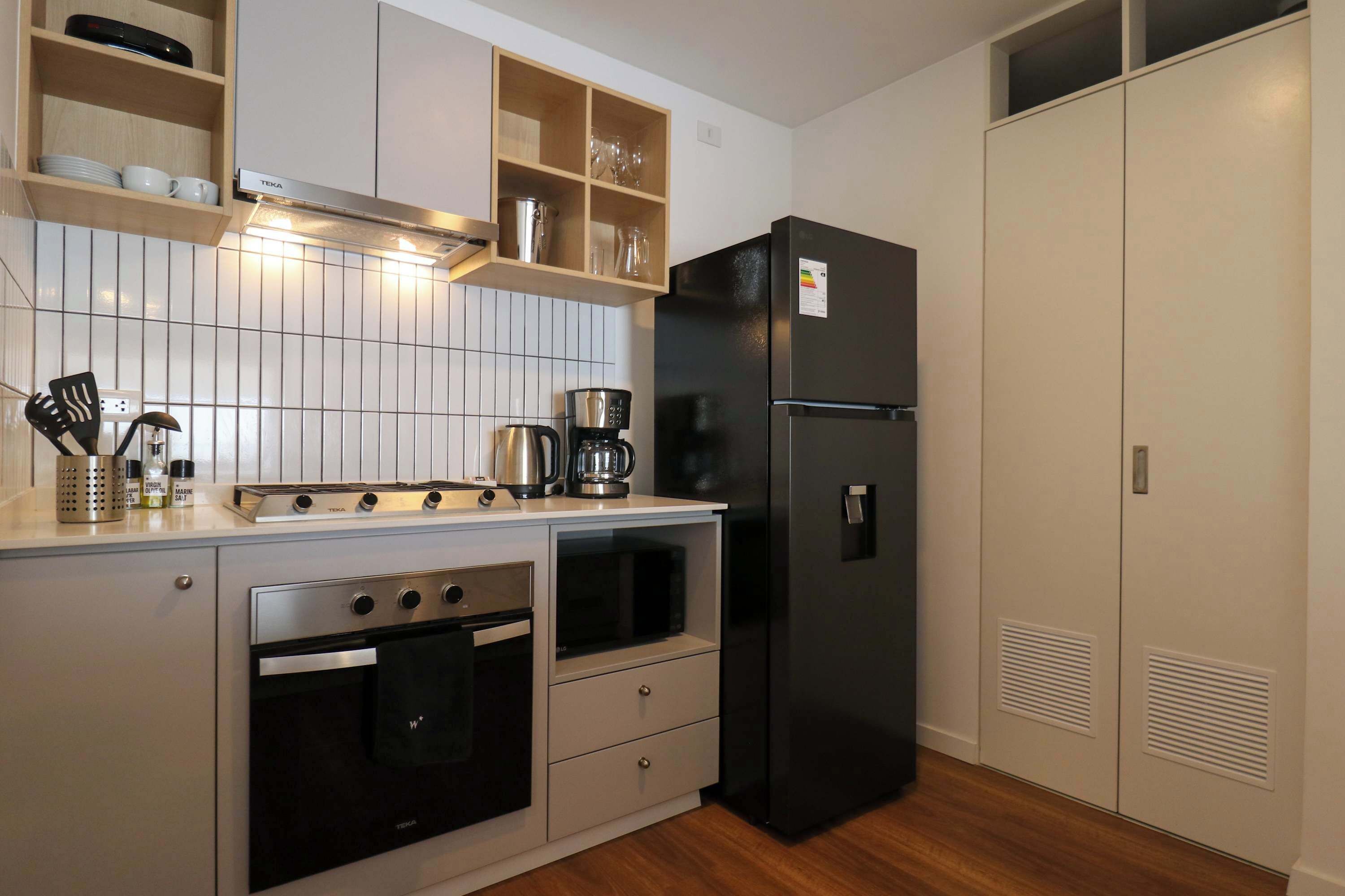 A compact kitchen with a stove, oven, microwave, coffee maker, and a black refrigerator.