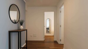 A hallway with wooden flooring, a black-framed mirror, and a white vase with a plant. - w* | Central 2BR w/ Balcony in Miraflores (Miraflores)