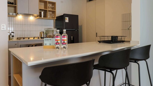 A modern kitchen with a white countertop, black chairs, and a black refrigerator. - w* | Central 2BR w/ Balcony in Miraflores (Miraflores)
