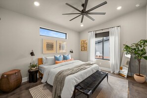 A bedroom with a bed, a ceiling fan, a window with curtains, a bedside table with a lamp, and a potted plant. - Cowboy Pool + Walk to Square | Sleeps 8 (Georgetown)