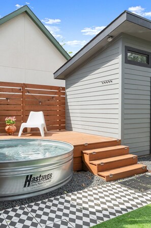 A backyard with a hot tub, wooden steps, a white plastic chair, and a checkered tile floor. - Cowboy Pool + Walk to Square | Sleeps 8 (Georgetown)