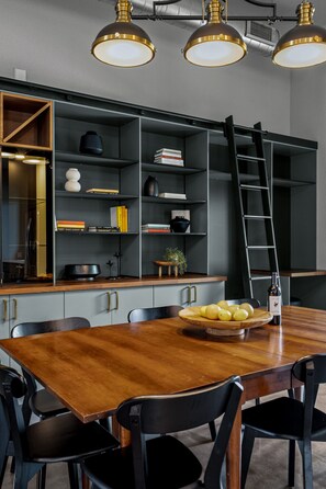 A modern kitchen with a wooden table, black chairs, and a built-in bookshelf.