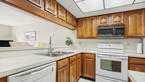 Una cocina con armarios de madera, microondas, horno y lavavajillas.