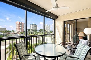 Un balcone con tavolo e sedie in vetro, una ventola a soffitto e vista su edifici alti.