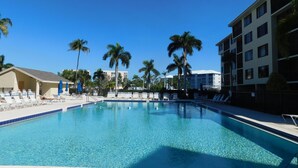 Una piscina con sillones de descanso y palmeras, rodeada de edificios.