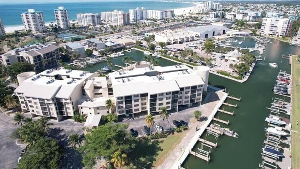 Un puerto deportivo con barcos, un edificio grande de varios pisos y una playa al fondo.