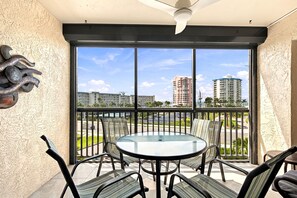 A balcony with a glass table and chairs, a ceiling fan, and a view of high-rise buildings. - 2-Bedroom, 2.5 Bath Condo in Sunny Fort Myers Beach Florida with Sunset Views (Fort Myers Beach)
