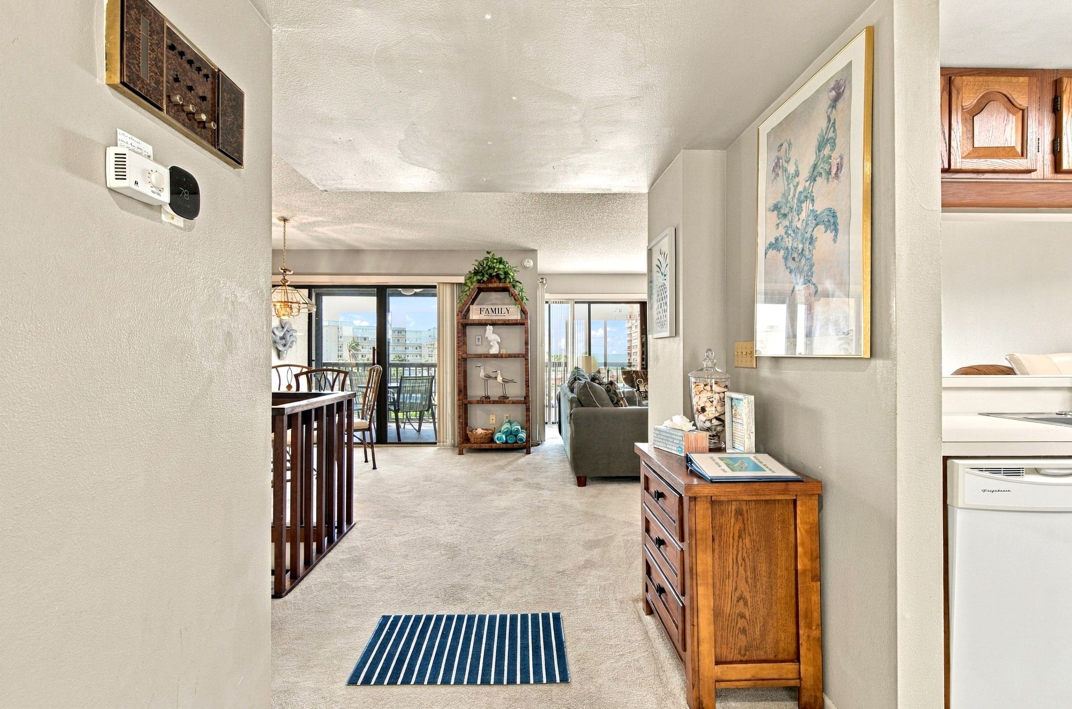 A spacious living area with a view to a balcony, a wooden cabinet, and a dining area with a striped rug.