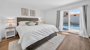 A bedroom with a bed, nightstands, a lamp, a window with curtains, and a view of a swimming pool.
