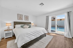 Ein Schlafzimmer mit Bett, Nachttischen, einer Lampe, einem Fenster mit Vorhängen und Blick auf einen Swimmingpool.