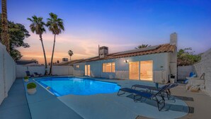 A swimming pool with lounge chairs, a building with large windows, and palm trees.