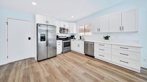 A modern kitchen with white cabinets, stainless steel appliances, and a wooden floor.