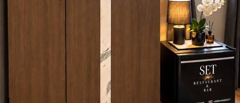 A wardrobe with a marble stripe, a small table with a lamp and orchid, and a black cabinet with SET restaurant and bar signage.