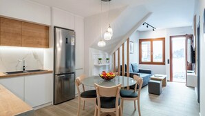Eine moderne Küche mit einem Edelstahl-Kühlschrank, einem runden Glastisch mit Stühlen und einer kleinen Sitzecke mit Sofa und Fenster.