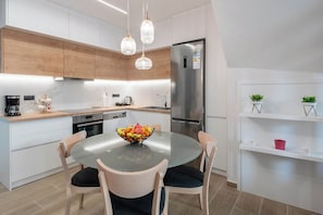 A modern kitchen with a round glass table, white cabinetry, and a stainless steel refrigerator. - Aurelia Suite - Old Town Escape ,  Rethymno 2-bedroom apartment (Rethymno)