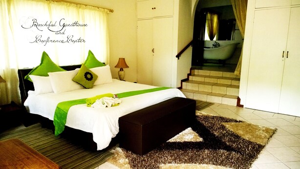Une chambre d’hôtel comprenant un lit, une table de chevet, une lampe, une salle de bain avec baignoire et un escalier.