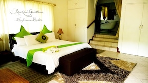Habitación de hotel con cama, mesita de noche, lámpara, baño con bañera y una escalera.