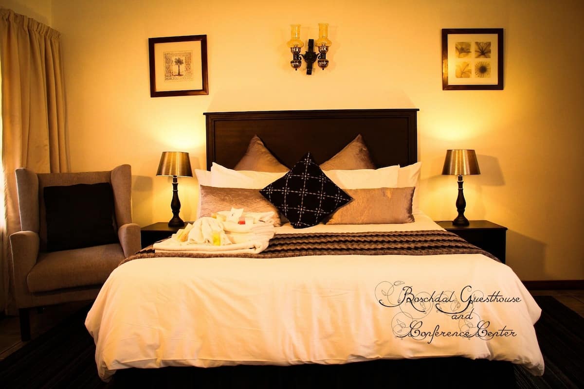 Una habitación de hotel con una cama, dos mesitas de noche, una silla y lámparas de pared.
