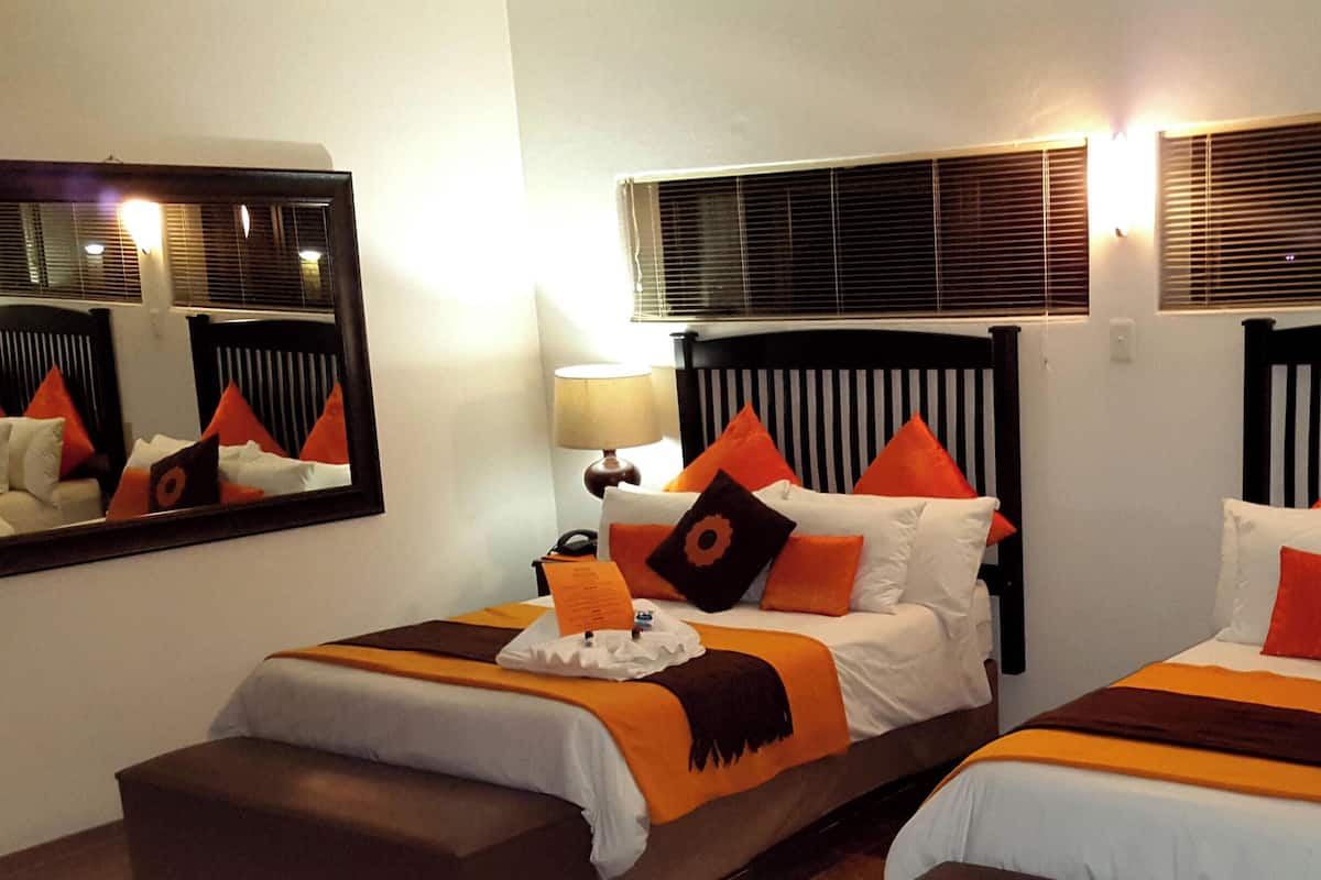 Habitación de hotel con dos camas, cada una con cabecero, mesita de noche, lámpara y espejo.