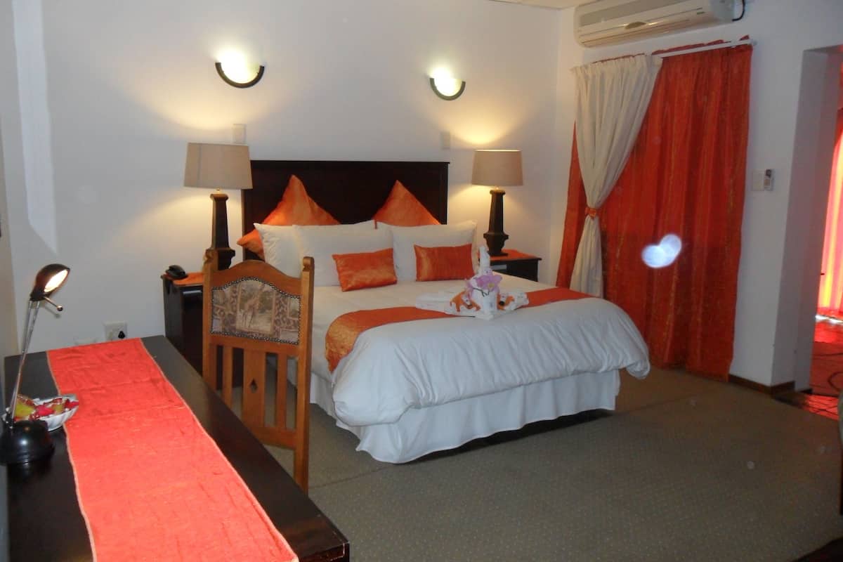 Habitación de hotel con cama, dos lámparas de noche, una mesita de noche, un escritorio con lámpara y una cortina roja.