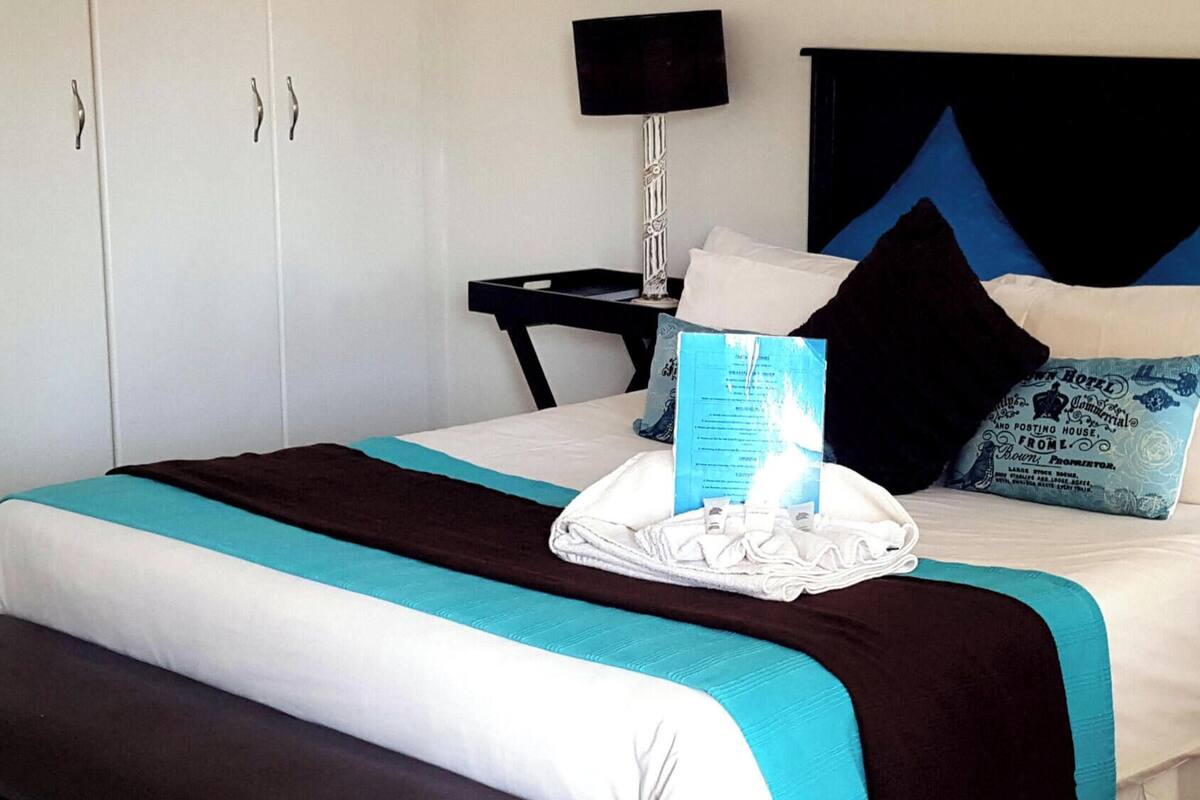 Una habitación de hotel con cama, un refrigerador pequeño, mesitas de noche y una silla.