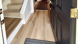 Un couloir avec un escalier en bois, une porte noire et un tapis à motifs.