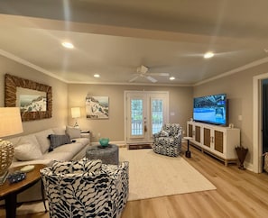 Una sala de estar con sofá, sillón estampado, televisor y una puerta con vistas.