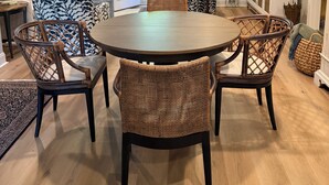 Un coin repas avec une table ronde et des chaises en osier, un canapé et un téléviseur posé sur un meuble.