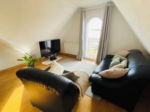 Ein modernes Wohnzimmer mit einem schwarzen Ledersofa, einem Flachbildfernseher und einer Topfpflanze.