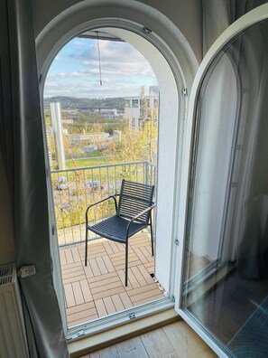 Ein Balkon mit einem Stuhl und Blick auf eine Wohngegend, im Hintergrund ein Gebäude.