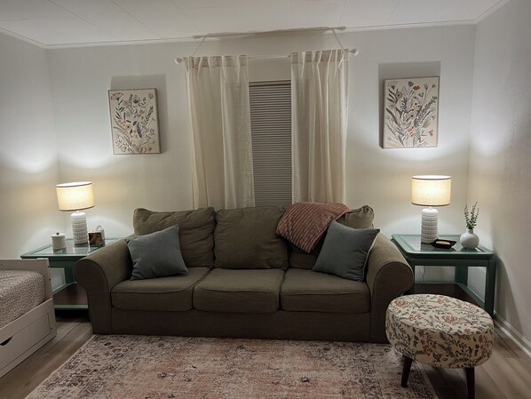 A cozy room with a green sofa, two side tables with lamps, a patterned rug, and floral artwork on the walls. - Wonderful 2-bedroom house with large backyard in peaceful Belleville. (Belleville)
