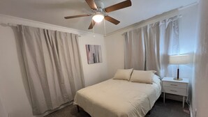 A bedroom with a bed, a nightstand, a lamp, a ceiling fan, and a painting on the wall.