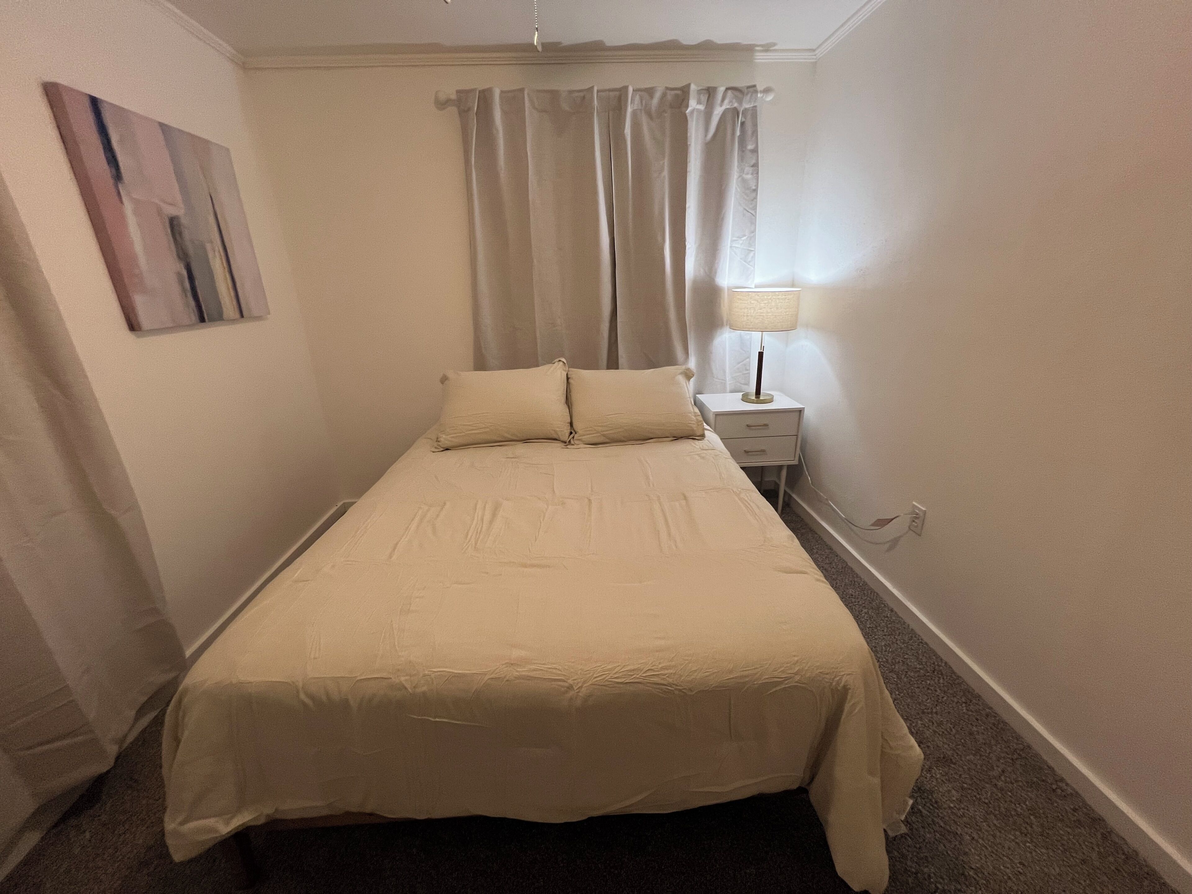 A single bed with a headboard, a bedside table with a lamp, and a painting on the wall.