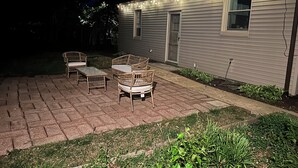A patio with wicker furniture, a brick floor, and a house with string lights.