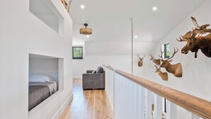 A modern interior with a wooden staircase, a bed with a view, and mounted animal heads on the wall. - 3-bedroom barn in gorgeous Folkston with AC for relaxing stays (Folkston)