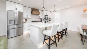 A modern kitchen with stainless steel appliances, white cabinetry, and a central island with bar stools. - 3-bedroom barn in gorgeous Folkston with AC for relaxing stays (Folkston)