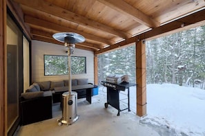 Un intérieur en bois avec un canapé, un coin barbecue et une grande fenêtre.