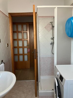 Un bagno con porta in legno, doccia, lavatrice e lavandino.