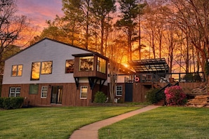 A two-story house with a large deck, a covered outdoor area, and a view of the sunset.