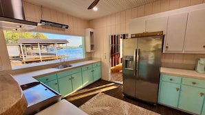 A kitchen with teal cabinets, a stainless steel refrigerator, a window with a view of a dock and water, and a ceiling fan. - 8 bdrm covered dock, bar and kitchen on the water! hot tub, firepit, sleeps 26, (Henrico)