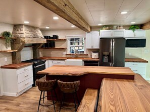 A kitchen with a wooden island, white cabinets, a stainless steel refrigerator, and a stone accent wall.