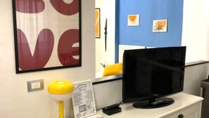 Une pièce avec une commode blanche, une lampe jaune, un téléviseur noir posé sur le dessus, un panneau décoratif avec le mot « AMOUR » et un mur d’accent bleu.